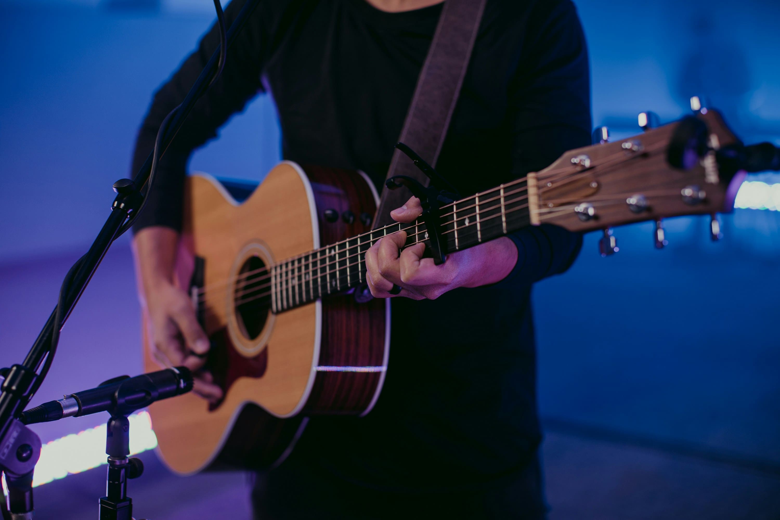 A person playing an acoustic guitar in front of a blue background.