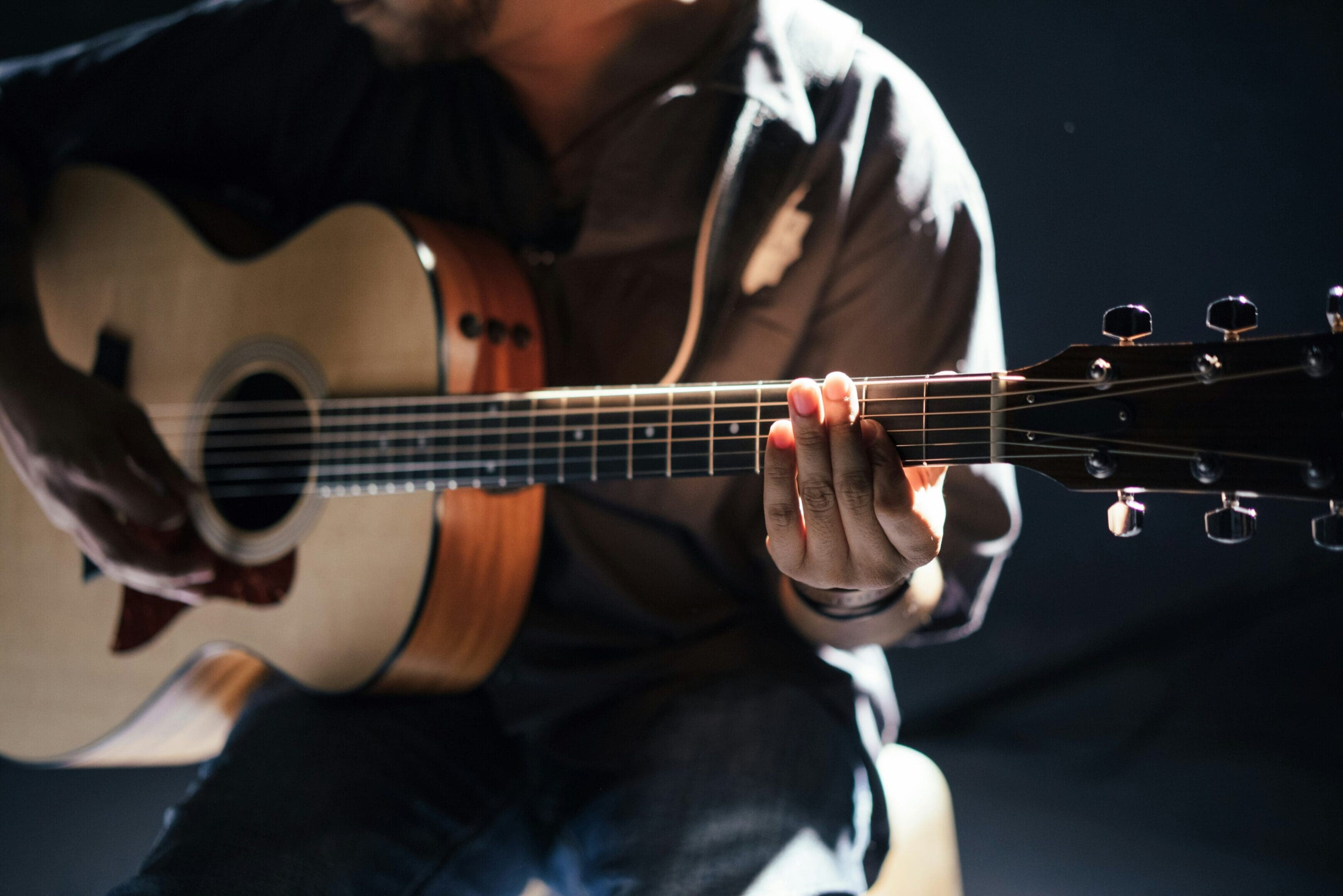 A person playing an acoustic guitar in the dark.